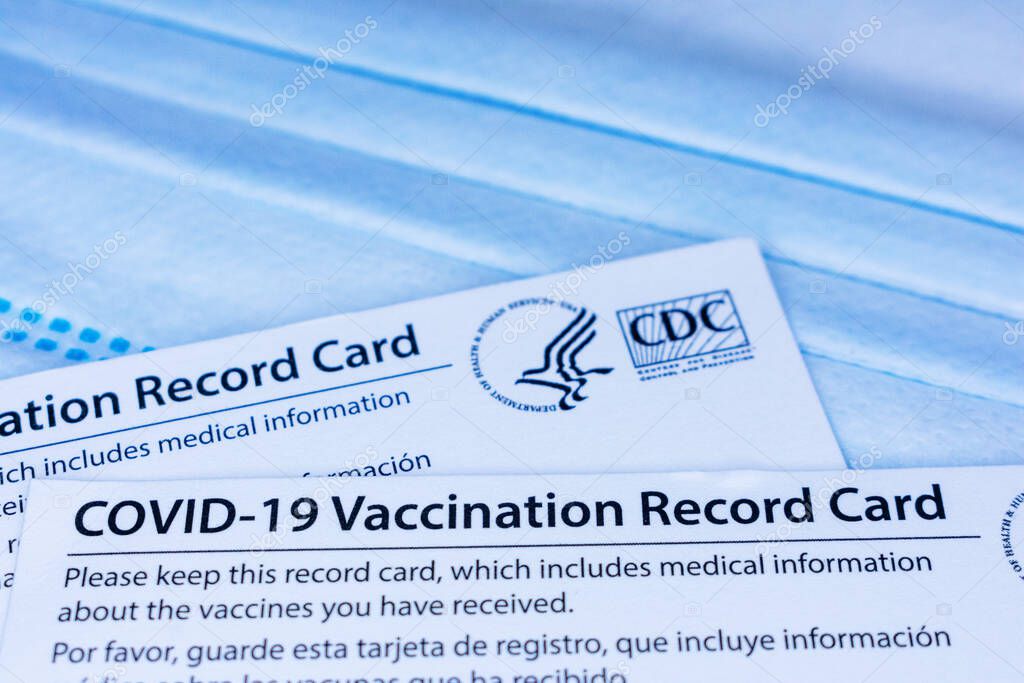 Closeup. Covid-19 vaccination record cards issued by CDC, United States Centers for Disease Control and Prevention, on a blue disposable face mask - San Jose, California, USA - 2021