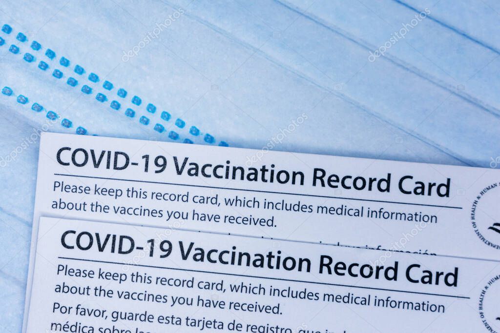 Closeup. Covid-19 vaccination record cards issued by CDC, United States Centers for Disease Control and Prevention, on a blue disposable face mask - San Jose, California, USA - 2021