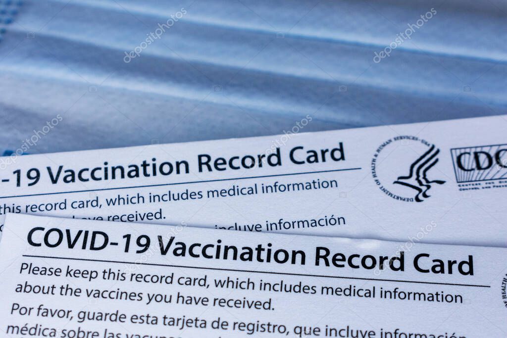 Closeup. Covid-19 vaccination record cards issued by CDC, United States Centers for Disease Control and Prevention, on a blue disposable face mask - San Jose, California, USA - 2021