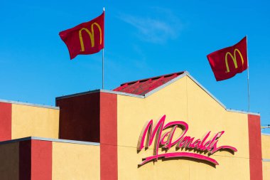 McDonald 's fast food zinciri restoran cephesi mavi gökyüzünün altında iki bayrakla. - Santa Clara, Kaliforniya, ABD - 2021