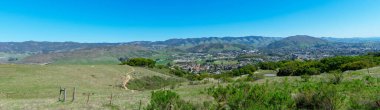 Elevated panoramic scenic view of San Luis Obispo urban area sprawl and green mountains of Santa Lucia Range from Bishop Peak Trail on sunny spring day. clipart