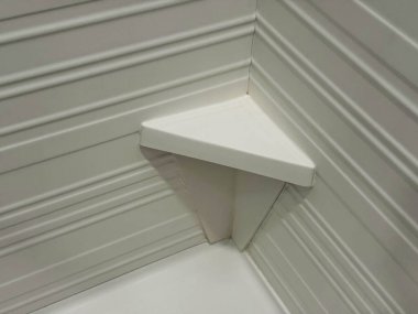 Beyaz duş köşesi üçgen raf ve destekli destekler dokulu duvar panelleri, işlevselliği, geometriyi ve temiz modern stili vurgulayan minimalist banyo tasarımı