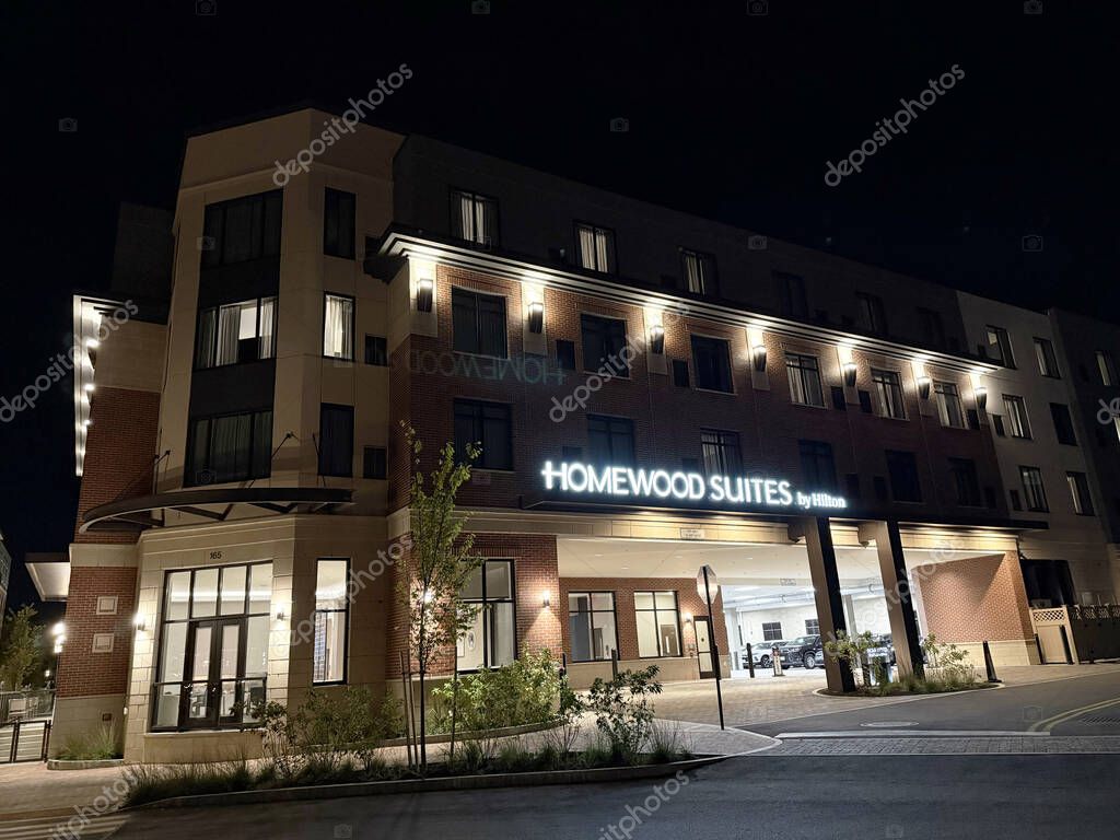 Night view of Homewood Suites by Hilton hotel building with glowing sign, parked cars - Portsmouth, New Hampshire, USA - October 2, 2025