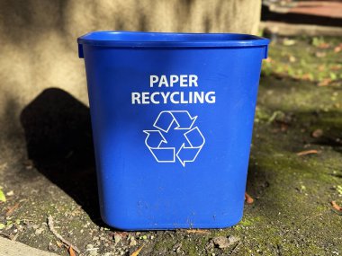 Blue plastic recycling bin labeled Paper Recycling with white recycling symbol placed outdoors