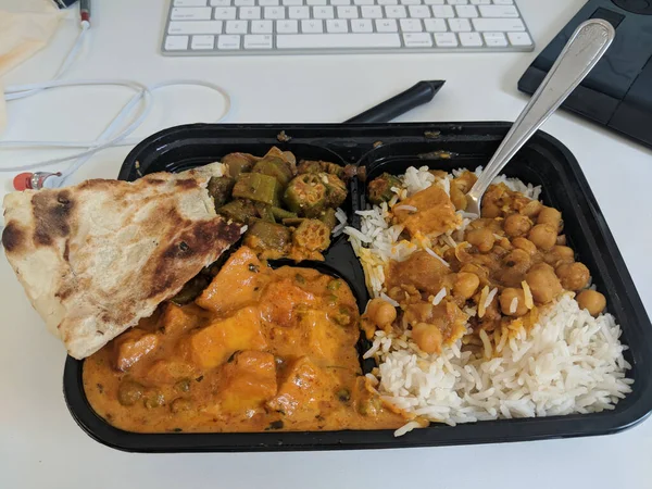Eating indian food in container during working. Chickpeas, rice, naan in plastic container on a computer desk