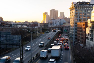 Otoyol yukarıdan görünüyor. Uzaktan geçen arabalar ve binalar var. Gün batımında Brooklyn otoyolunda araba sürmek.