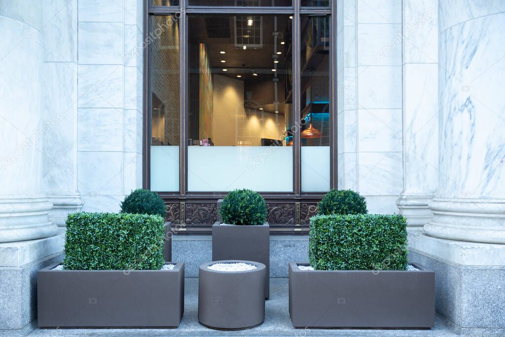 Big gray, metal planters with foliage plants and terrace design with a modern mix of construction material. Bushes against a building with big window