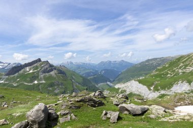 Arka planda dağlar, çayırlar, çimenler ve güzel, güneşli bir günde kayalar olan panoramik dağ manzarası.