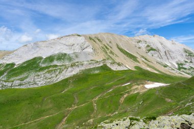 Arka planda dağlar, çayırlar, çimenler ve güzel, güneşli bir günde kayalar olan panoramik dağ manzarası.