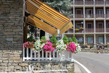 Courmayeur, İtalya - 24 Ağustos 2021: Sarı çizgili, çizgili tente restoranın üzerinde çitin etrafında çiçeklerle yemek için açık alan