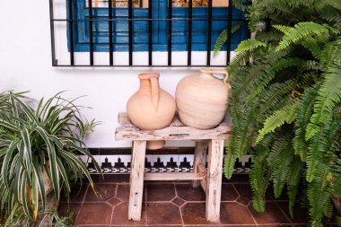 two terracotta amphora resting on a wooden stool in a courtyard