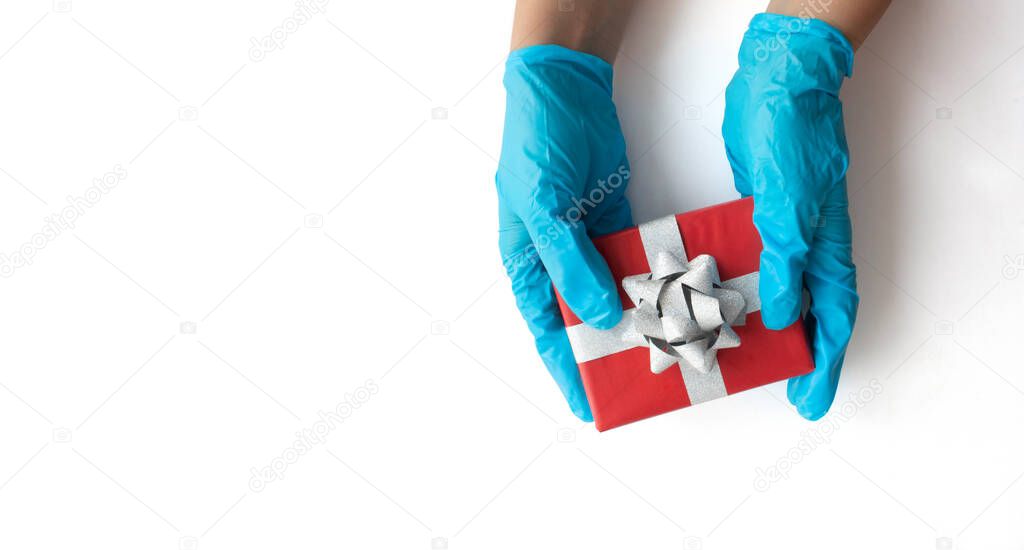 Gloved hands carefully hold the wrapped gift on a white background with copy space. Safe home delivery. The concept of safe delivery in the context of the COVID-19 pandemic.