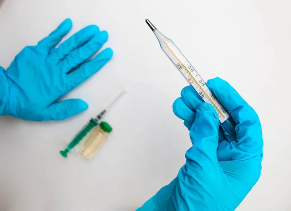 Les mains des médecins tiennent un thermomètre, dans le fond un vaccin et une seringue. - Le concept de recherche médicale avant vaccination. — Photo