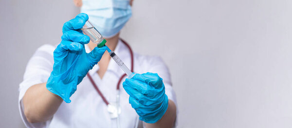 A nurse wearing protective gloves and a mask dials a vaccine into a syringe, the concept of vaccinating the population against coronavirus, influenza, and SARS.