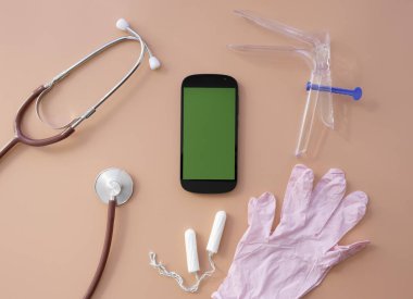 a layout with medical instruments, tampons, and a phone on a pink background.