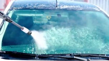 Cleaning the car, using a high-pressure washer, in the open air. Windshield and roof washing.