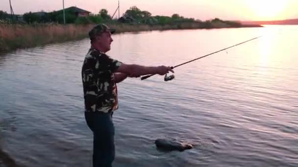 Silhouette d'un pêcheur, un homme pêchant dans la rivière au coucher du soleil. — Video