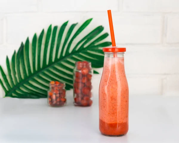 Still life with a bottle of berry smoothie, berries in jars, and a branch of palm — Stock Photo, Image