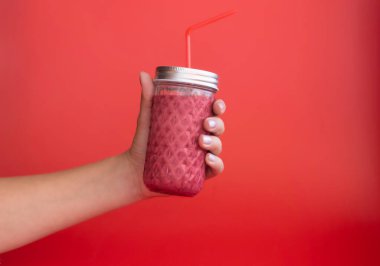 El, tek renkli kırmızı arka planda bir kavanoz meyve püresi tutuyor.