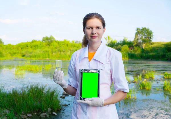 Laboratorieassistenten står på stranden av behållaren med ett vattenprov och en tablett, begreppet ekologi — Stockfoto
