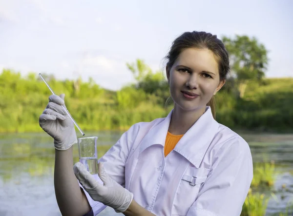 Girl laboratory assistant looks at a sample of water in a test tube, recruited from the lake, the concept of ecology Stock Picture