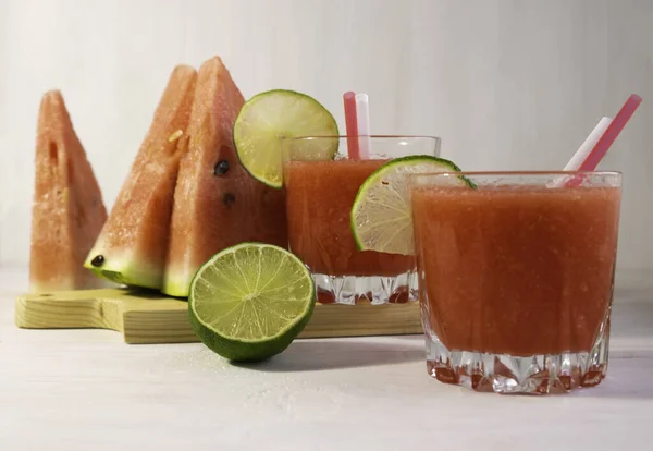 Two glasses of watermelon cocktail, and slices of watermelon and lime on a white background — Stock Photo, Image