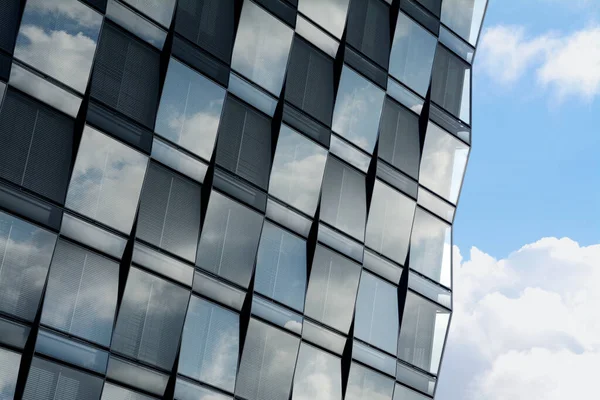 Mavi gökyüzünde ve bulutlarda kristal gökdelen. Damalı pencerelerde Venedik panjurları var.