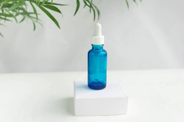 Beyaz bir podyumda yeşil tropikal yapraklı beyaz bir zeminde doğal kozmetik ürünleri için mavi cam kavanoz. Moda minimalist soyut koleksiyonu. Bir kadının güzelliği. Doğal arkaplan.