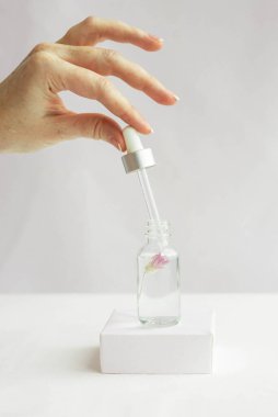 Beyaz bir podyumda beyaz bir arka planda doğal kozmetik için cam kavanoz ve içinde kadın eli olan bir çiçek. Moda minimalist soyut koleksiyonu. Bir kadının güzelliği. Doğal arkaplan.