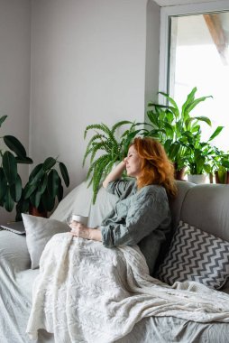 Yükümlü bir kadın kanepeye oturur, battaniyeyle kaplanır ve lezzetli bir fincan çay, kahve ya da kakao ile dinlenir. Evde sabah eğlencesi, ahenkli zihinsel durum, sakinlik, dinlenme, rahatlama.