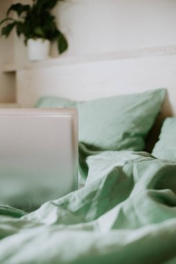 Dizüstü bilgisayar, keten çarşaflı bir yatakta. Bilinçli yaşam konsepti, evden çalışma, uzaktan çalışma, serbest çalışma, köy hayatı..