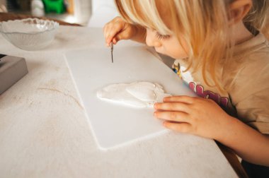 Ailesine ve akrabalarına sürpriz olsun diye kilden bir hediye çıkaran küçük bir çocuğun elleri. Çocuk gelişimi, hobiler, kil hobisi. Elle yapılmış. Sıcak ev atmosferi.