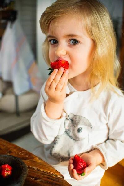 Little child girl eats fresh ripe strawberries in the morning at breakfast. Home garden, healthy food, childs diet. — Stock Photo, Image