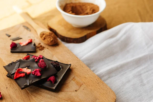 Tavoletta di cioccolato con fragole su tavola di legno con ciotola bianca con cacao in polvere e cucchiaio di legno Foto Stock