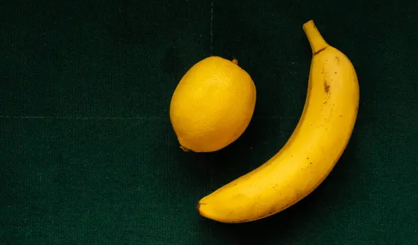 Banane und Zitrone auf smaragdgrünem Hintergrund, gesunde Ernährung — Stockfoto