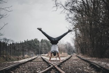 Demiryolu raylarında kollarında duran genç adam.