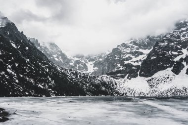 Donmuş bir gölün kıyısında karla kaplı güzel dağlar.