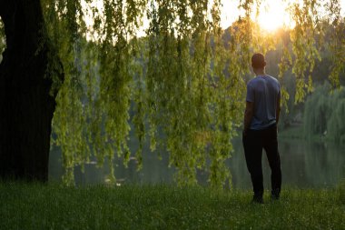 Gölde düşünceleri olan genç bir adam. Kavram: Günbatımı, sükunet