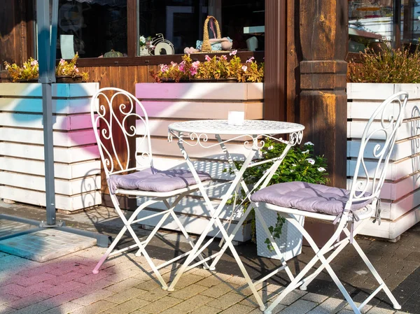 Boş beyaz masa ve bir kafe barın ya da güneş ışınları ve neon gölgeli bir restoranın önünde birkaç sandalye. Aşk ve romantik yemek kavramı.