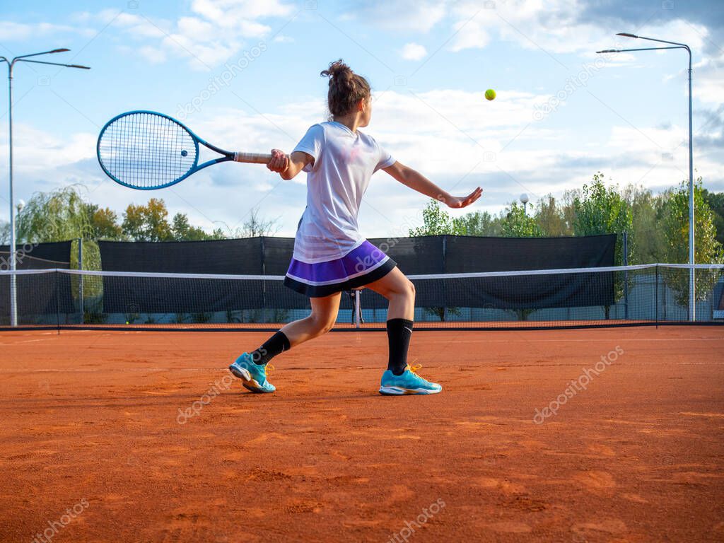 Tennis player. Beautiful girl teenager with racket hits ball on tennis court