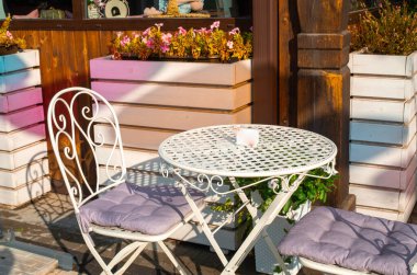 Boş beyaz masa ve bir kafe bar ya da restoranın dışındaki sokakta birkaç sandalye.