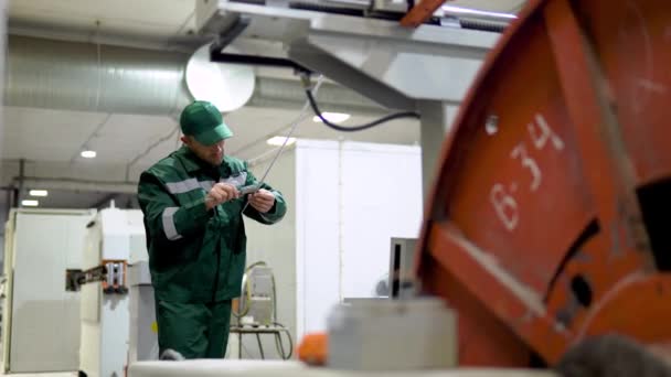 Trabajador de fábrica en una bata y gorra comprueba el rendimiento del dispositivo para la producción de productos de cable a partir de un núcleo de cobre — Vídeo de stock