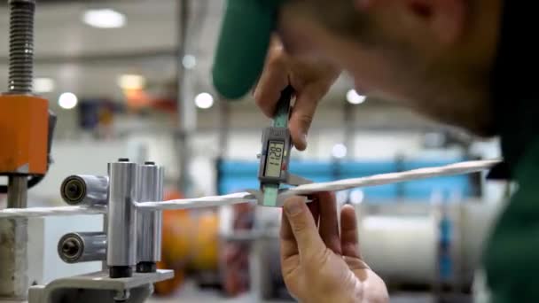 Trabalhador da fábrica em um manto e tampa verifica o desempenho do dispositivo para a produção de produtos de cabo a partir de um núcleo de cobre — Vídeo de Stock