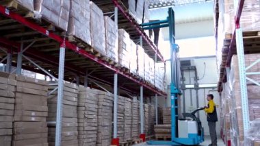 Forklift yükleyicisiyle karton kutular yükleyen üniformalı bir depo çalışanı.