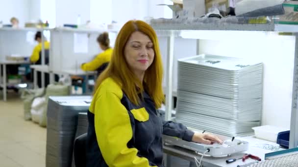 Portrait of red-haired woman factory worker sitting near production Assembly line at the plant for production of electrical products — Stock Video