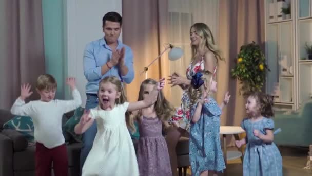 Lykkelig familie mor far og flere børn danser hjemme i festlige tøj. De fejrer deres fødselsdag have det sjovt og hoppe. – Stock-video