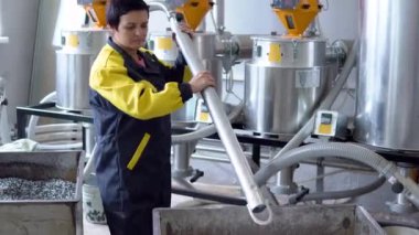 Üretim fabrikası işçisi, fabrika atölyesindeki tanktan beyaz bakir plastik granülleri emen hortumla çalışıyor.