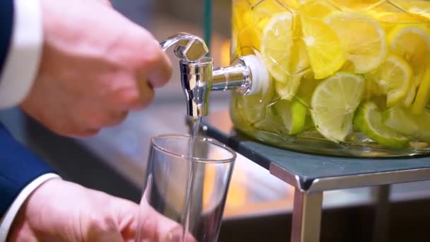 Mens hands pour water into a glass from a glass decanter with lemon and lime — Stock Video