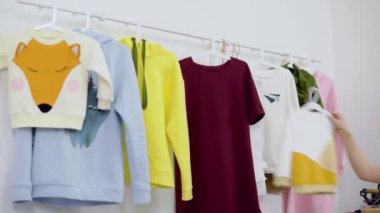 Kadın moda tasarımcısı yeni kadın giyim koleksiyonu üzerinde çalışıyor. Stüdyo atölyesi, terzi, terzi ya da nakışçı. Elbise rafının yanında şık el yapımı kıyafetlerle duruyor.