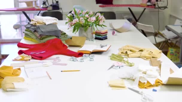 Aufnahme eines sonnigen Modedesignstudios mit verschiedenen Näharbeiten und bunten Stoffen auf dem Tisch — Stockvideo